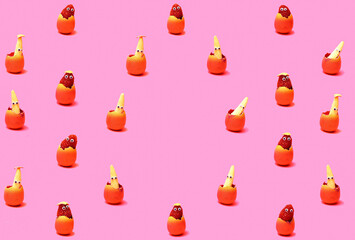 Pattern created of raspberry and baby corns with wiggle eyes in pink egg shell with egg shells on the bottom. Egg shaped copy space in the middle. Pink background.