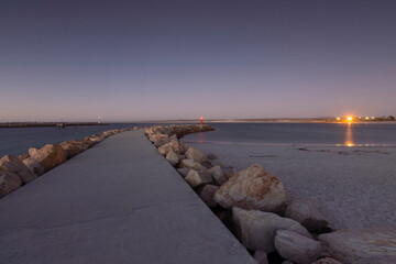 A harbor wall in Lambert's Bay, South Africa, with a lighthouse at the end of the wall, at dusk.