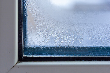 A fragment of a plastic window with condensation of water on the glass. Concept: defective plastic window with condensation, temperature difference, cooling, humidity in the room.