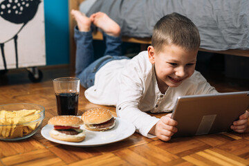 little boy digital tablet and eating junk food in his room