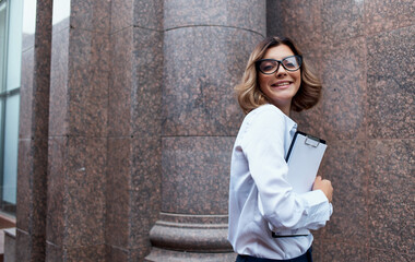 happy businesswoman near building with documents in hands and glasses on face cropped view