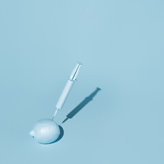 Monochrome visual of blue lemon and syringe on pastel blue background. Creative vaccine, coronavirus or GMO fruit concept. Genetically engineered food inspiration with trend summer shadows.