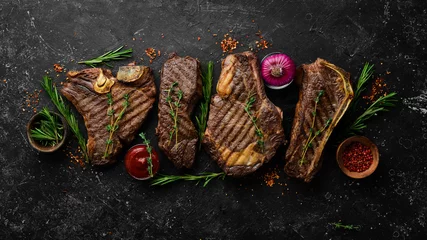 Foto op Canvas Steak menu. Juicy grilled steaks on a black stone background: t-bone, striploin, Rib eye, new york steak. Top view. Rustic style. © Yaruniv-Studio