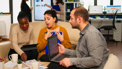Confident company manager giving working tasks to diverse teammates sitting on couch in start up...