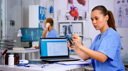 Medical doctor nurse holding and analysing radiography checking treatment of diagnosed patients, writing informations in laptop. Assistant working in hospital making appointments and registration.