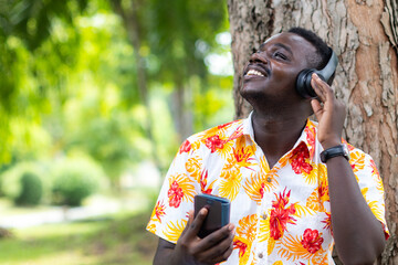 African man listening to music from smartphone with bluetooth or wireless earphones with smile and...