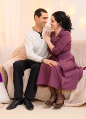 portrait of adult romantic couple sitting on a couch in home interior decorated with lights