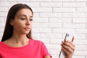 Young woman unlocking smartphone with facial scanner near white brick wall. Biometric verification