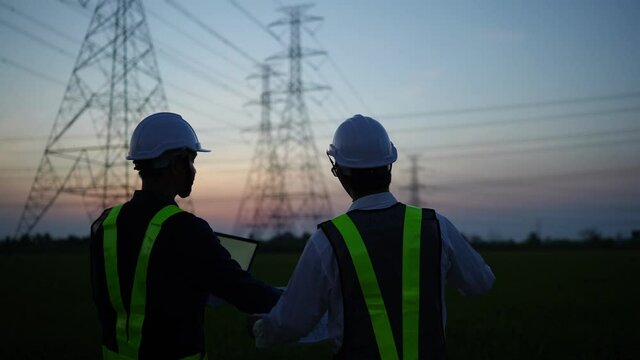 Two electrical engineers discussing a project on a high-voltage tower in the evening.