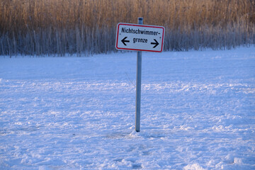 Ein Hinweisschild steht in einem zugefrorenen  See