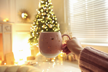 Woman with cup of drink and blurred Christmas tree on background, closeup