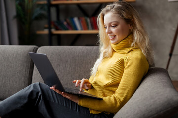 Beautiful young woman working from home on a laptop sitting on the sofa in the living room