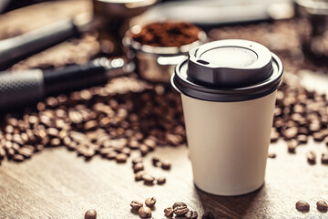 Paper takeaway cup with a plastic lid with a coffee with coffee beans and ground coffee in the background