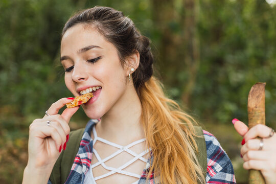 Portrait of a beautiful young woman eating a cereal bar in the forest.