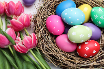Fototapeta na wymiar Colorful eggs in nest and tulips on white background, flat lay. Happy Easter