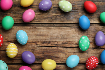 Fototapeta na wymiar Frame of colorful eggs on wooden background, flat lay with space for text. Happy Easter