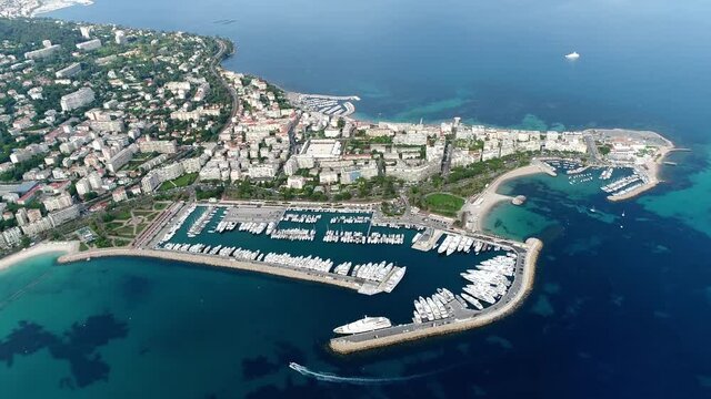 Aerial helicopter view of French Cannes Port Pierre Canto at the far end of the Croisette showing docked yachts and boats and in background further city buildings and coastline 4k high resolution