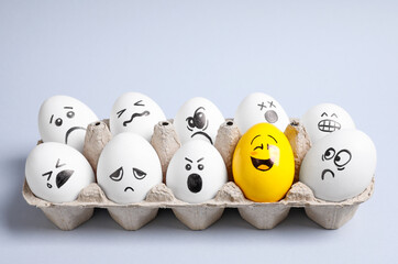 Yellow smiley egg among others with negative emotions in package on light background