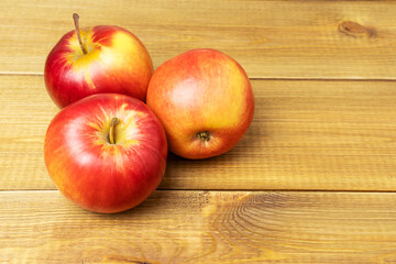 Three red ripe apples on wooden boards table.