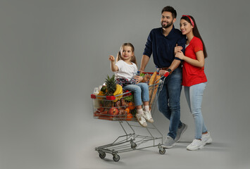 Happy family with shopping cart full of groceries on grey background