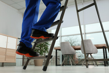 Professional worker climbing up ladder in room, closeup. Space for text