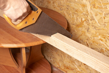 A male carpenter saws a wooden board with a hand saw. Repair of a house or apartment, construction and creation of furniture