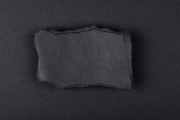Torn sheet of black paper on a black background.