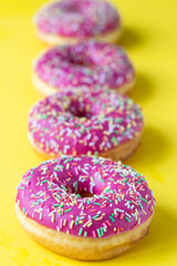 Pink glaze donuts with colorful sprinkles on yellow background. Minimalist concept.