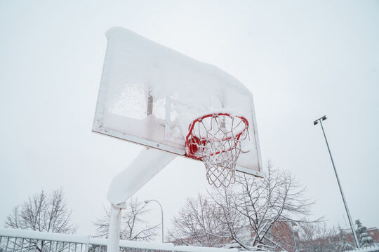 Horizontal view of frozen basketball court outdoors. Leisure in the park still not recovered from the snowstorm in Madrid in winter. Damages and insurance concept.