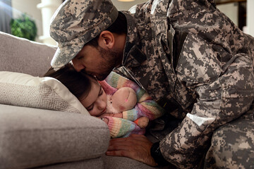 Soldier kissing his daughter while she sleeping on a bed at home.