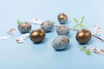 Easter Decoration with blue golden eggs, quail feathers, flowers on blue background. Happy Easter card concept.