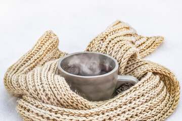 Hot tea with steam in a gray mug on the snow. 