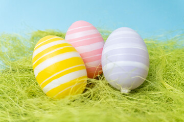 Easter painted eggs of light pastel tones lie in young grass, on a blue background