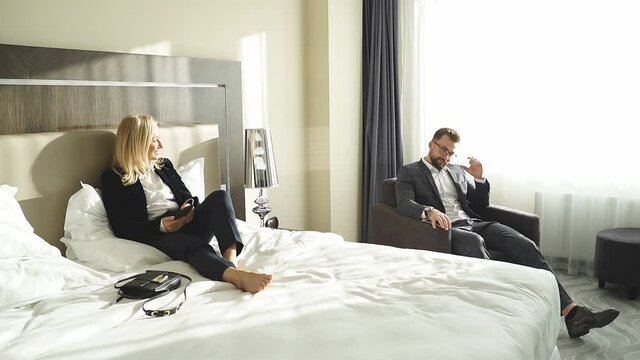 Man and woman arrived in hotel room, have rest after business meeting. woman lie on bed, happy to have rest.