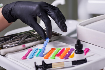 Close up of doctor hand in sterile glove grabbing blue orthodontic ligature tie. Dentist taking...
