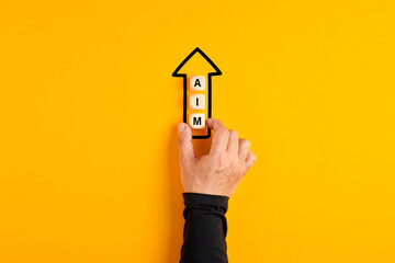 Male hand placing the wooden blocks with the word aim in an arrow pointing upwards on yellow...