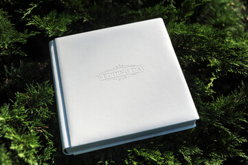 White leather wedding photo album with embossed cover lies on a green natural background