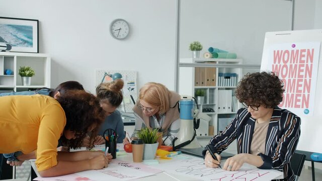 Multi-ethnic group of independent women are drawing posters for gender equality protest concentrated on creative activity. Feminism and girl power concept.