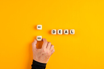 The word deal on wooden blocks with a male hand choosing the yes option. To accept a business deal