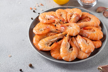 Boiled shrimps in a round plate and spices on a light gray background. Copy space