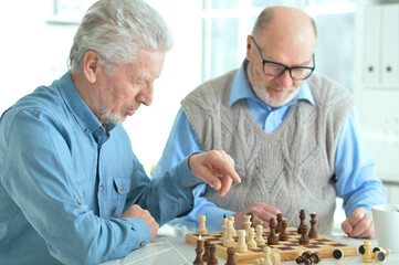 two senior couples sitting at table and playing chess