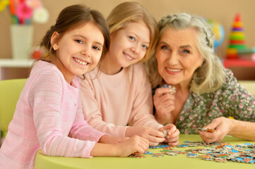 Grandmother with little granddaughters collecting  puzzle