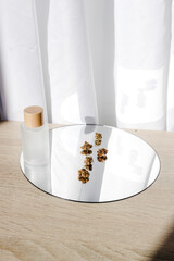 Cannabis and beauty oil product packaging on a mirror, and their shades on a white satin silky background.