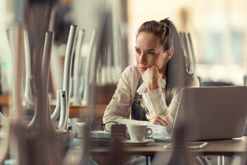 Unhappy female pub owner sits over computer and coffee thinking about what to do as business are...
