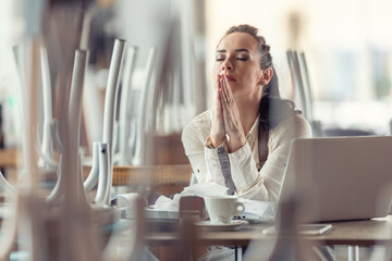 Businesswoman in a closed cafe prays with eyes closed for better times
