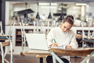 Female restaurant chef sits at the table after hours doing her bookkeeping in front of an open...