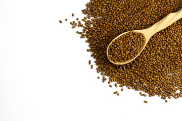Buckwheat tea in a wooden spoon on a white background copy space. Isolate. Buckwheat tea close-up macro photography. Scattered buckwheat tea pellets on white background top view.