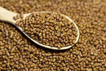 Buckwheat tea in a wooden spoon. Buckwheat tea close-up macro photography. Scattered buckwheat tea pellets brown background.
