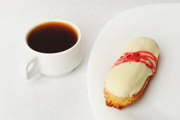 Appetizing strawberry french eclair with creamy icing on a white plate. Cup of coffee, pure white background
