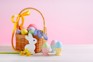Basket with flowers and decorated eggs for the Easter holiday. Colorful eggs in egg stands. Homemade rabbit cookies